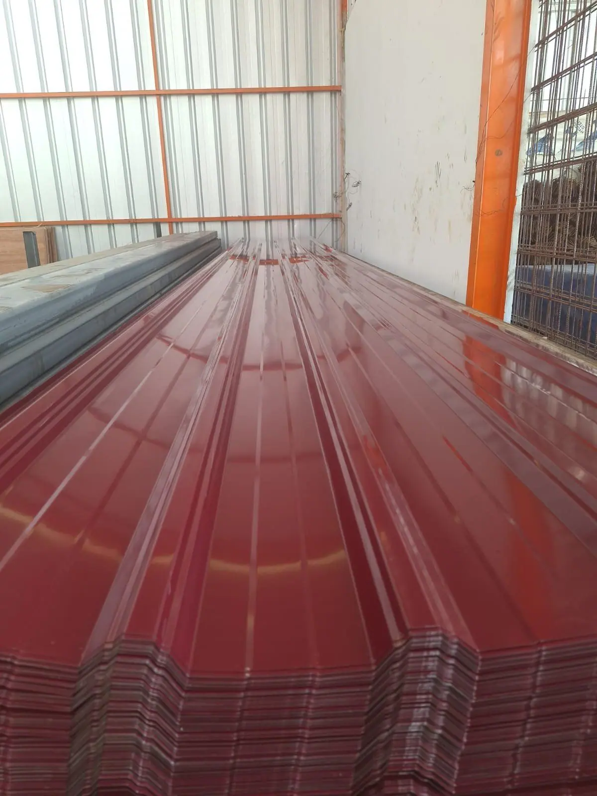 Tumpukan atap spandek merah di gudang dengan rangka oranye